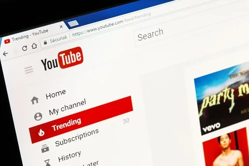 A computer screen displaying the YouTube homepage with the "Trending" section highlighted in red. The image represents YouTube's interface, navigation menu, and trending content section.